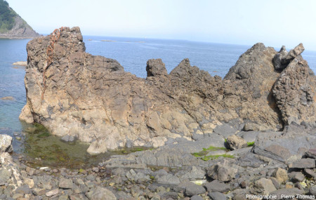 Vue d'ensemble d'un secteur montrant le contact entre des sédiments pélitiques sombres (au premier plan) recouvrant le haut d'une coulée basaltique (au deuxième plan) altérée et jaunâtre, Armitza, Pays basque espagnol
