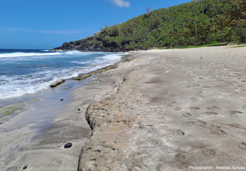 Détail du sable de la plage de Grande Anse (La Réunion), vue en direction du Nord, avec une falaise littorale en fond formant le Cap de l'Abri