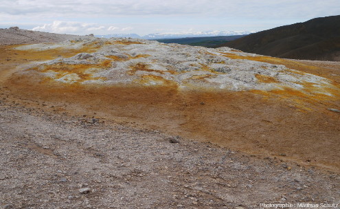 Zone vivement colorée par les dépôts fumerolliens sur la crête Námafjall (Islande), et sommets enneigés à l'horizon
