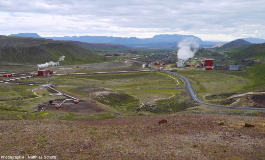 Forages, conduites forcées, tours de refroidissement et bâtiments rouges vifs de la centrale géothermique du Krafla (Islande), prise depuis les pentes Sud du volcan